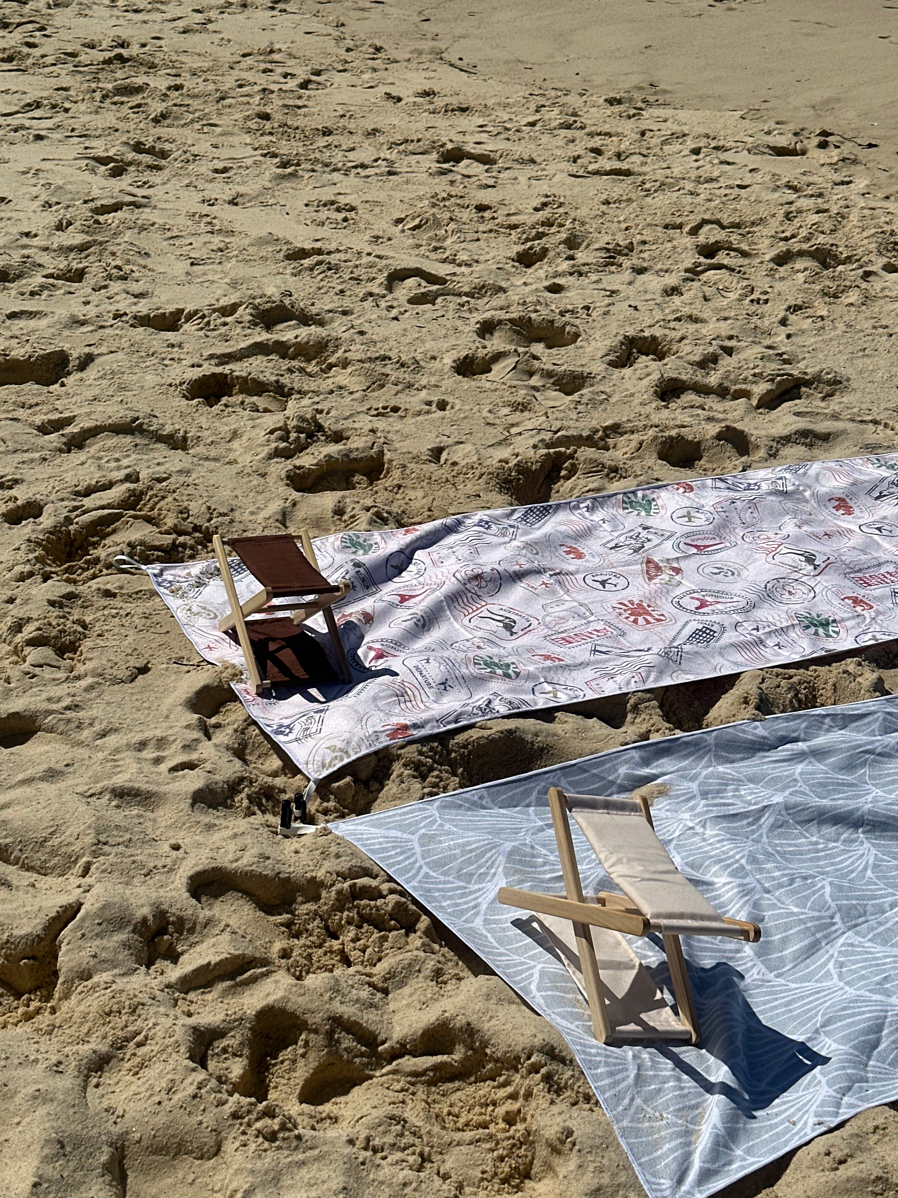 A beach headrest in two stunning colours resting on the sand beside sand-free beach towels—your perfect companion for relaxing, travel, and sunny beach days.
