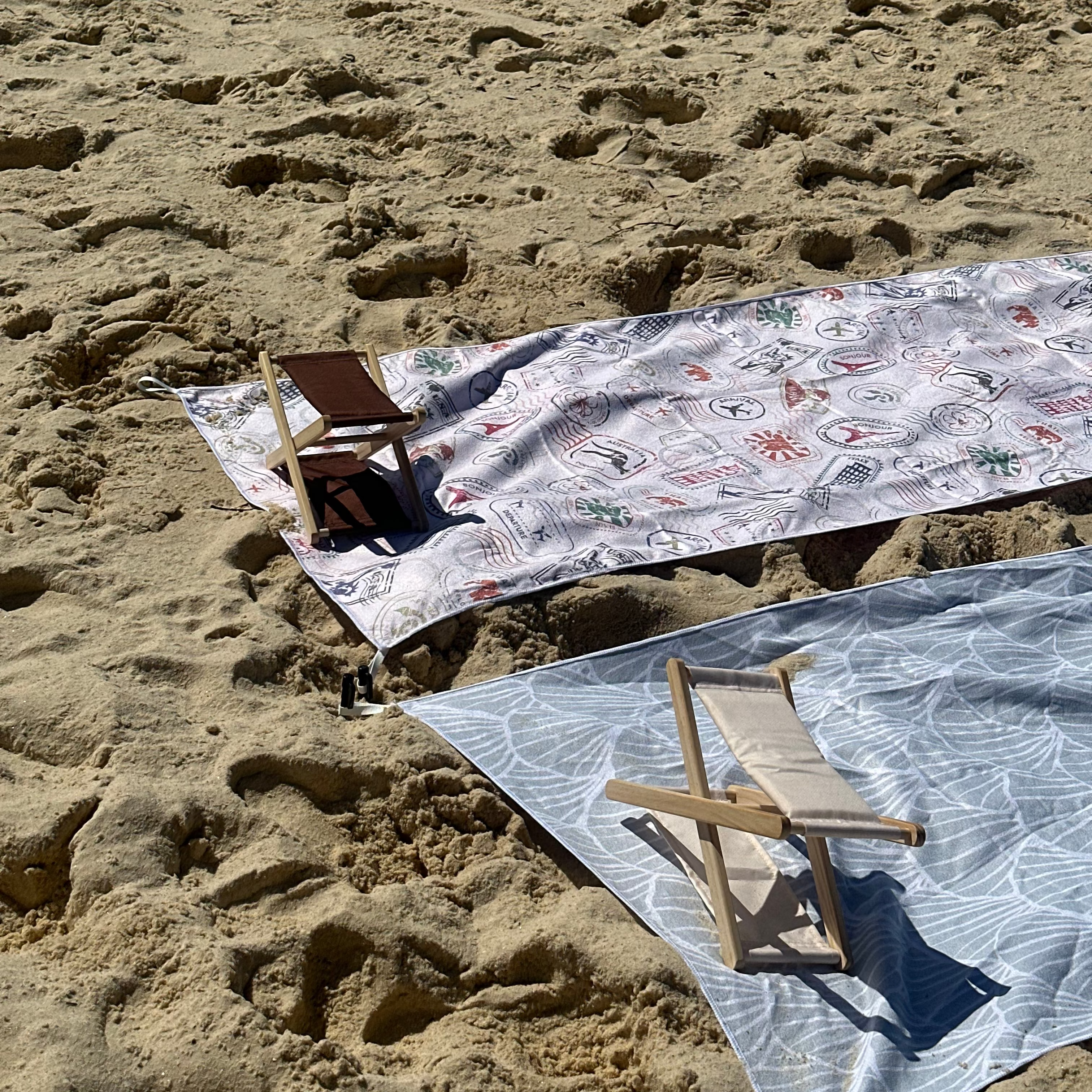 A beach headrest in two stunning colours resting on the sand beside sand-free beach towels—your perfect companion for relaxing, travel, and sunny beach days.