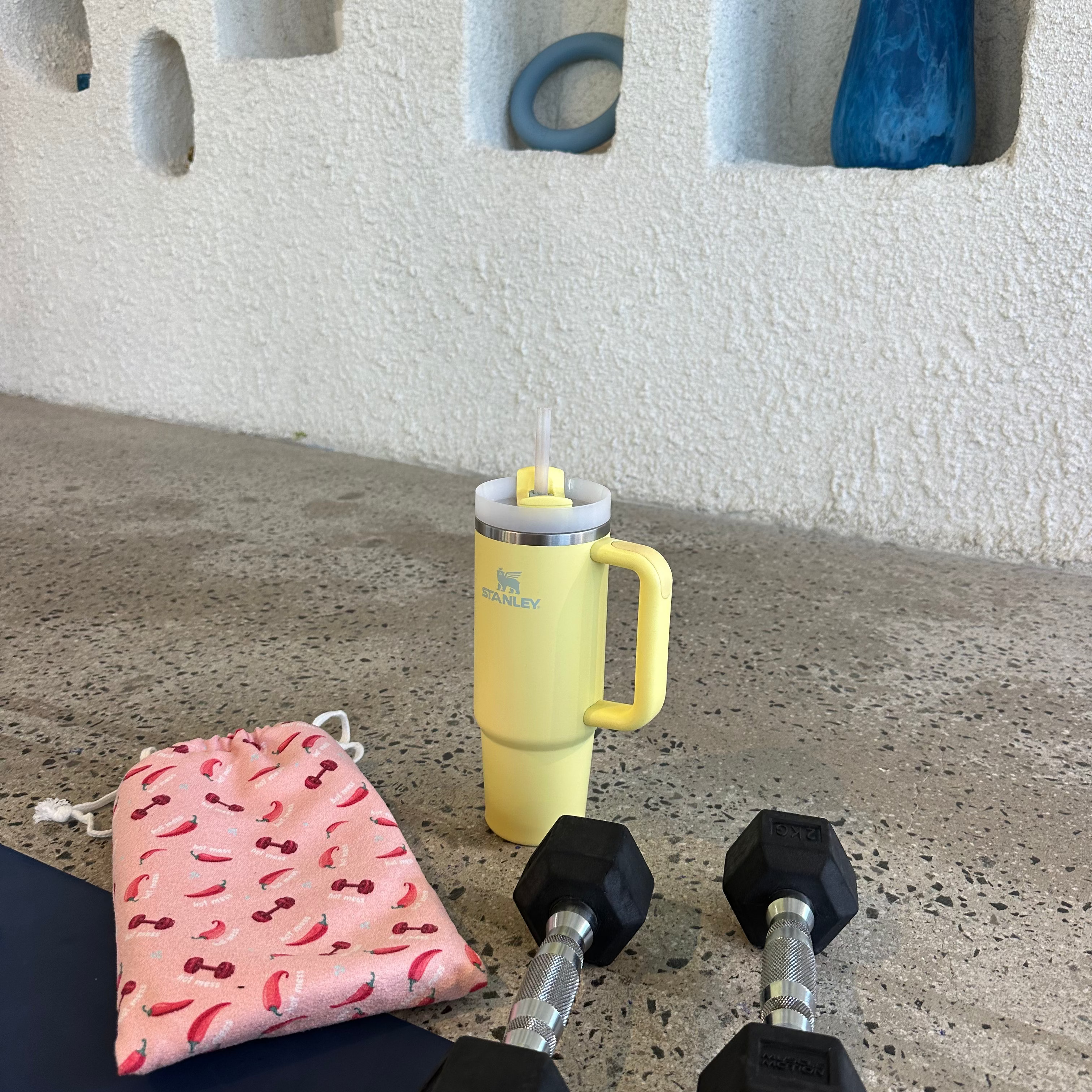 A simple, colourful home workout scene with light weights, Stanley for hydration, and a cute gym towel bag with a playful pattern of red chili peppers and small dumbbells comes with Hood and Pocket
