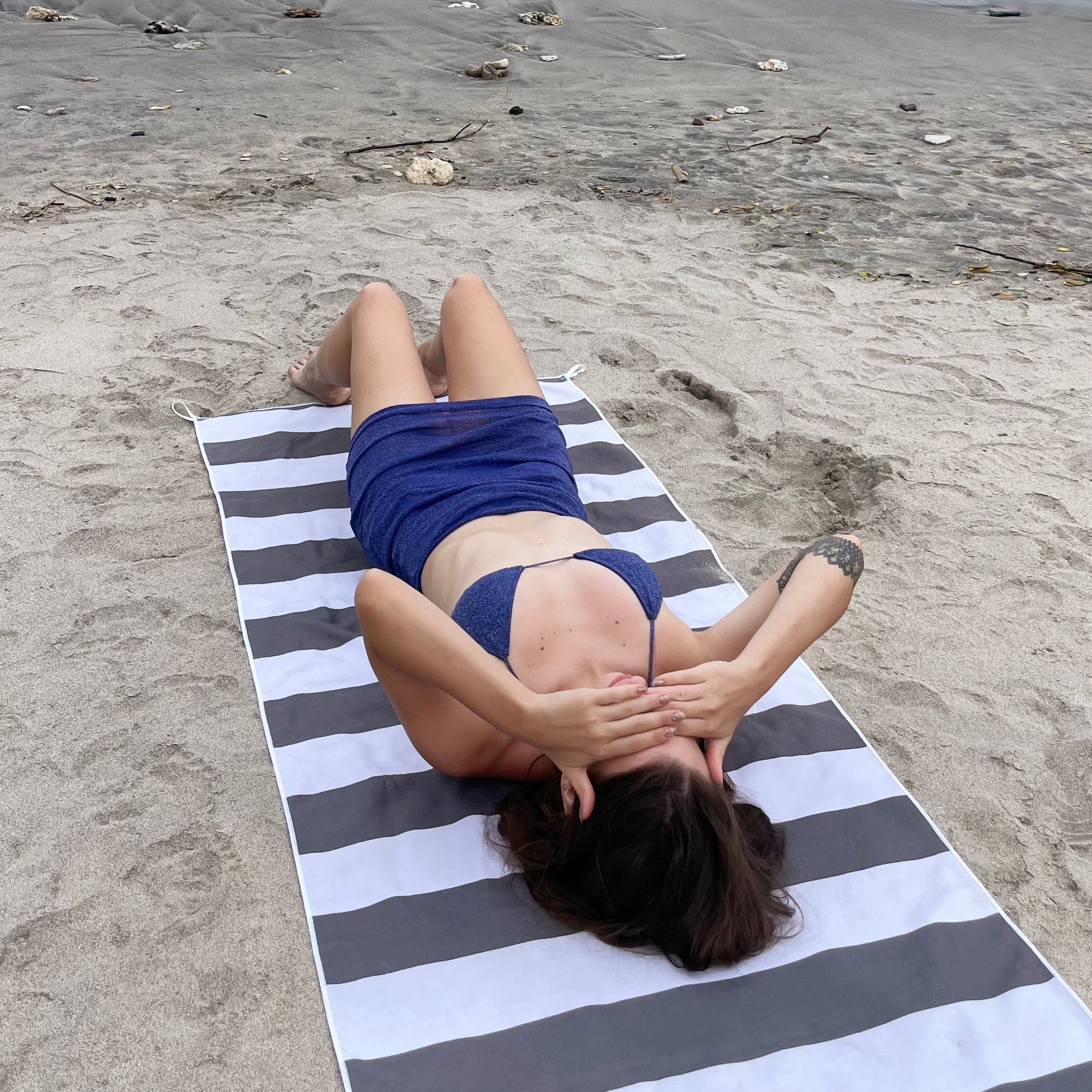 Person lying on a striped towel at the beach with a small island in the background