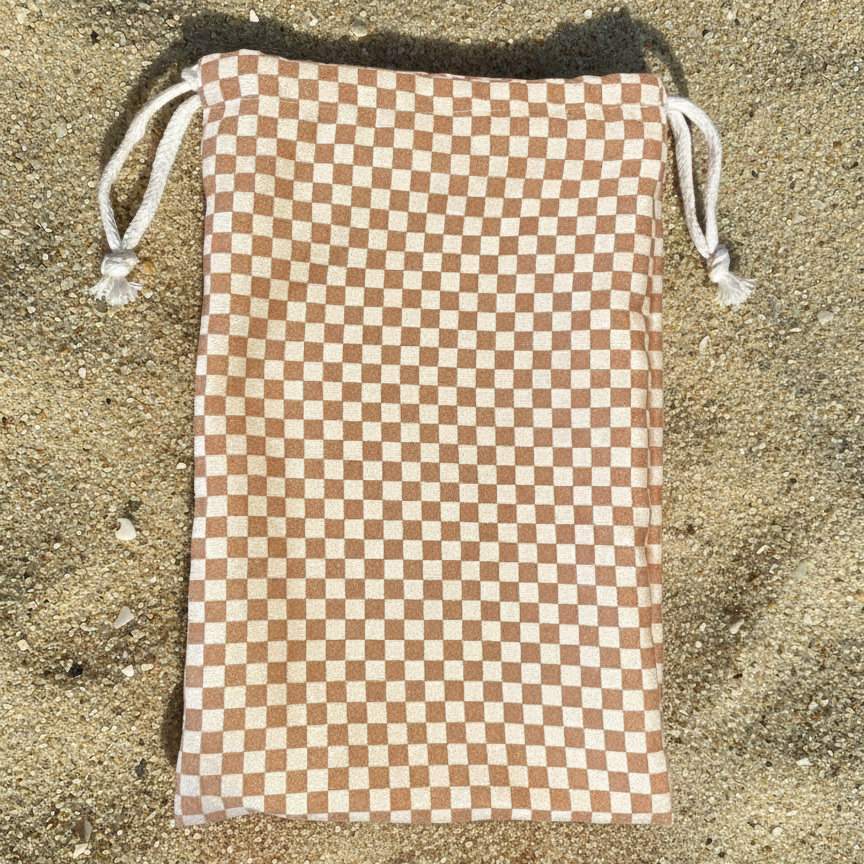 The colours are warm and earthy, combining a soft cream or off-white base with medium, sandy brown squares that echo the surrounding beach tones.